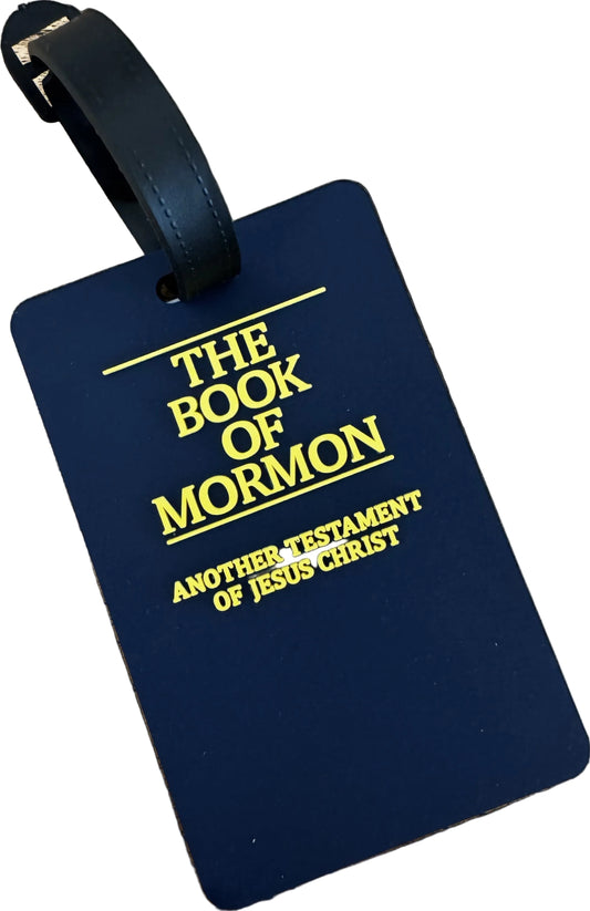 A dark blue luggage tag with a black strap, featuring the text 'THE BOOK OF MORMON' and 'ANOTHER TESTAMENT OF JESUS CHRIST' printed in yellow on a black background.